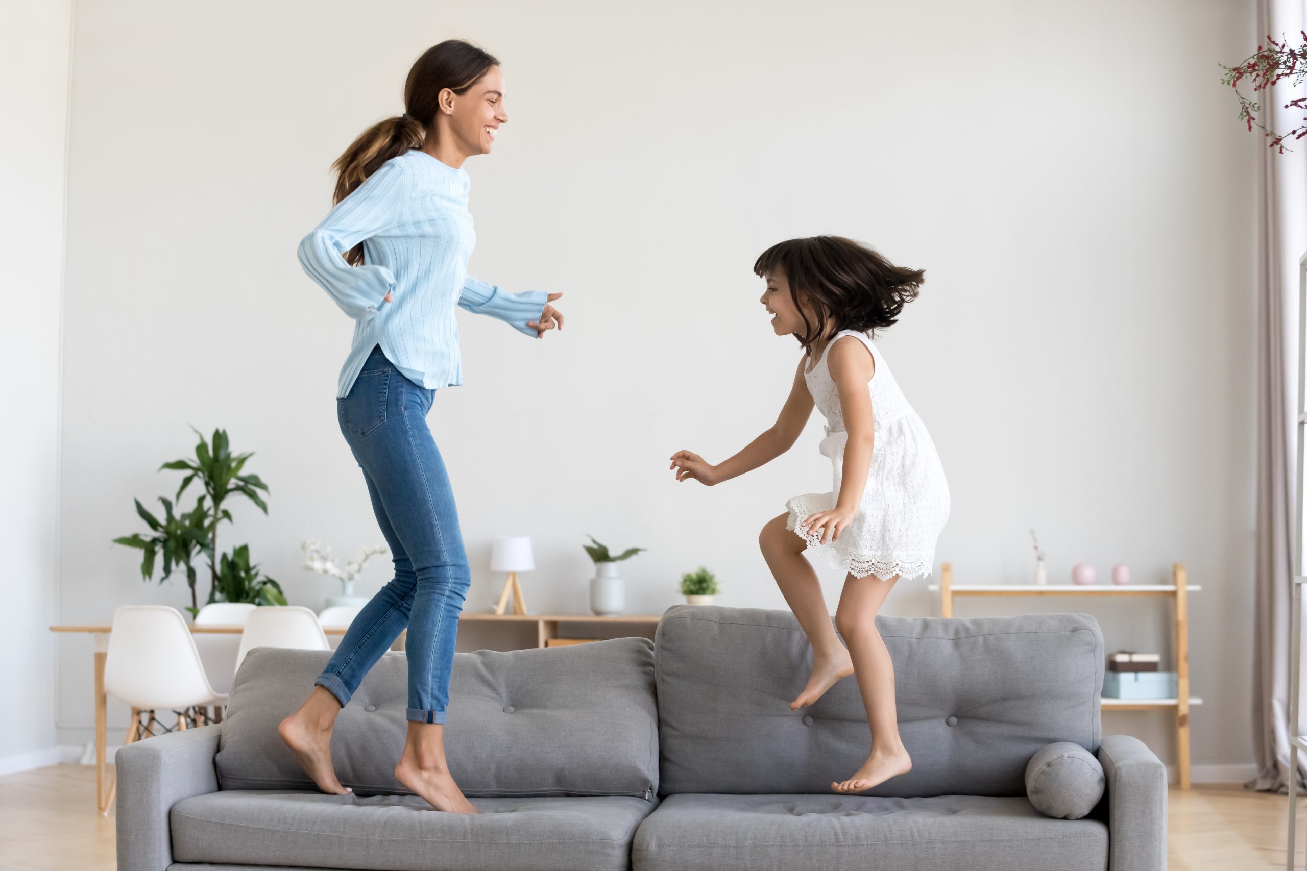 Happy mum and little daughter playing jumping on comfortable sof